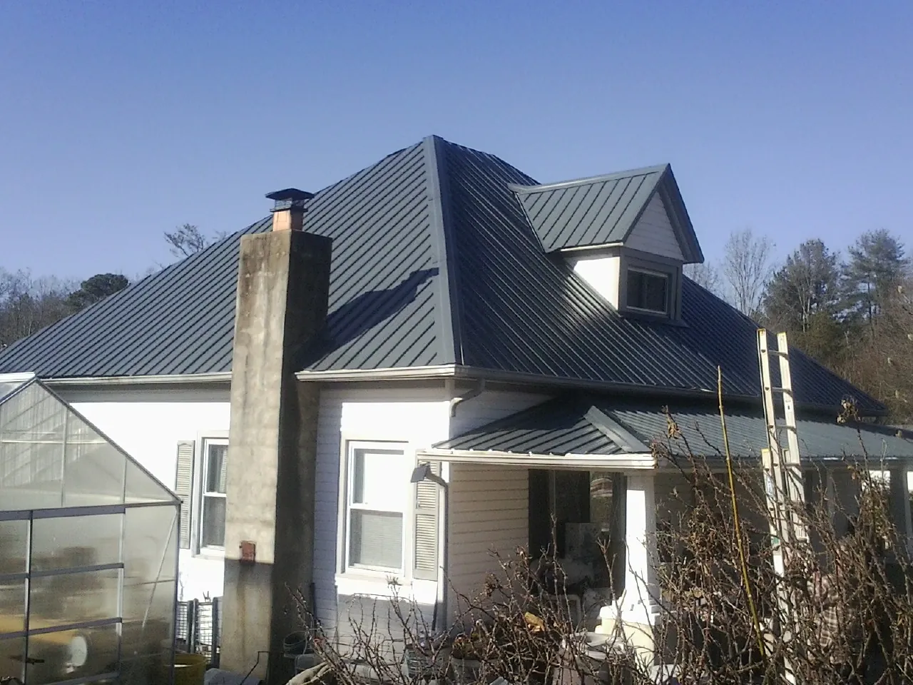 Dark blue standing seam metal roof on a white farmhouse with dormer — Slate & Tile Roof Repair by Roofing Brothers in Oquawka