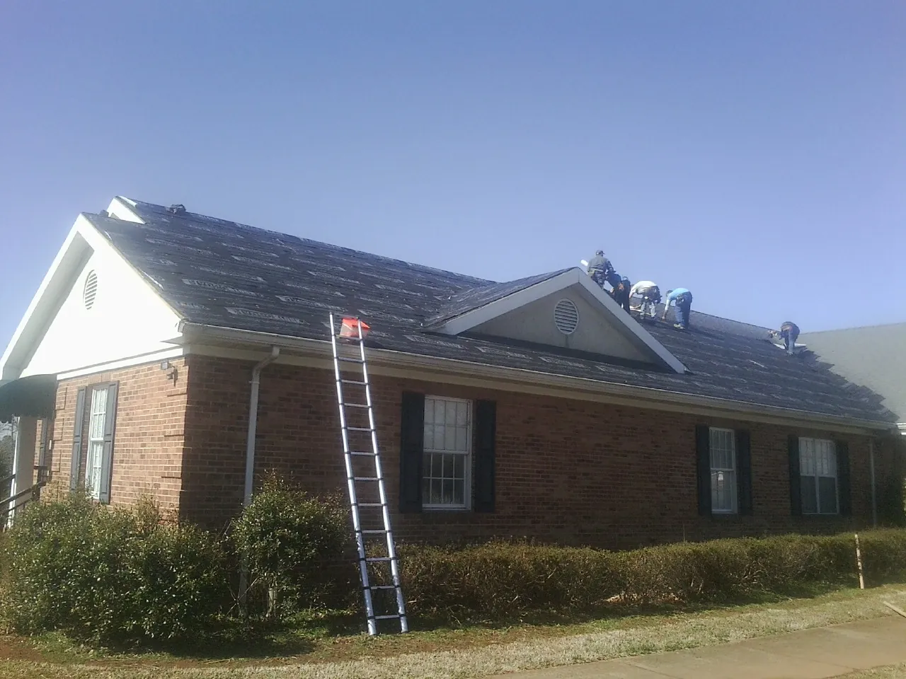 Crew tearing shingles off a brick ranch roof with a ladder set — Emergency Roof Repair work by our crew in Oquawka