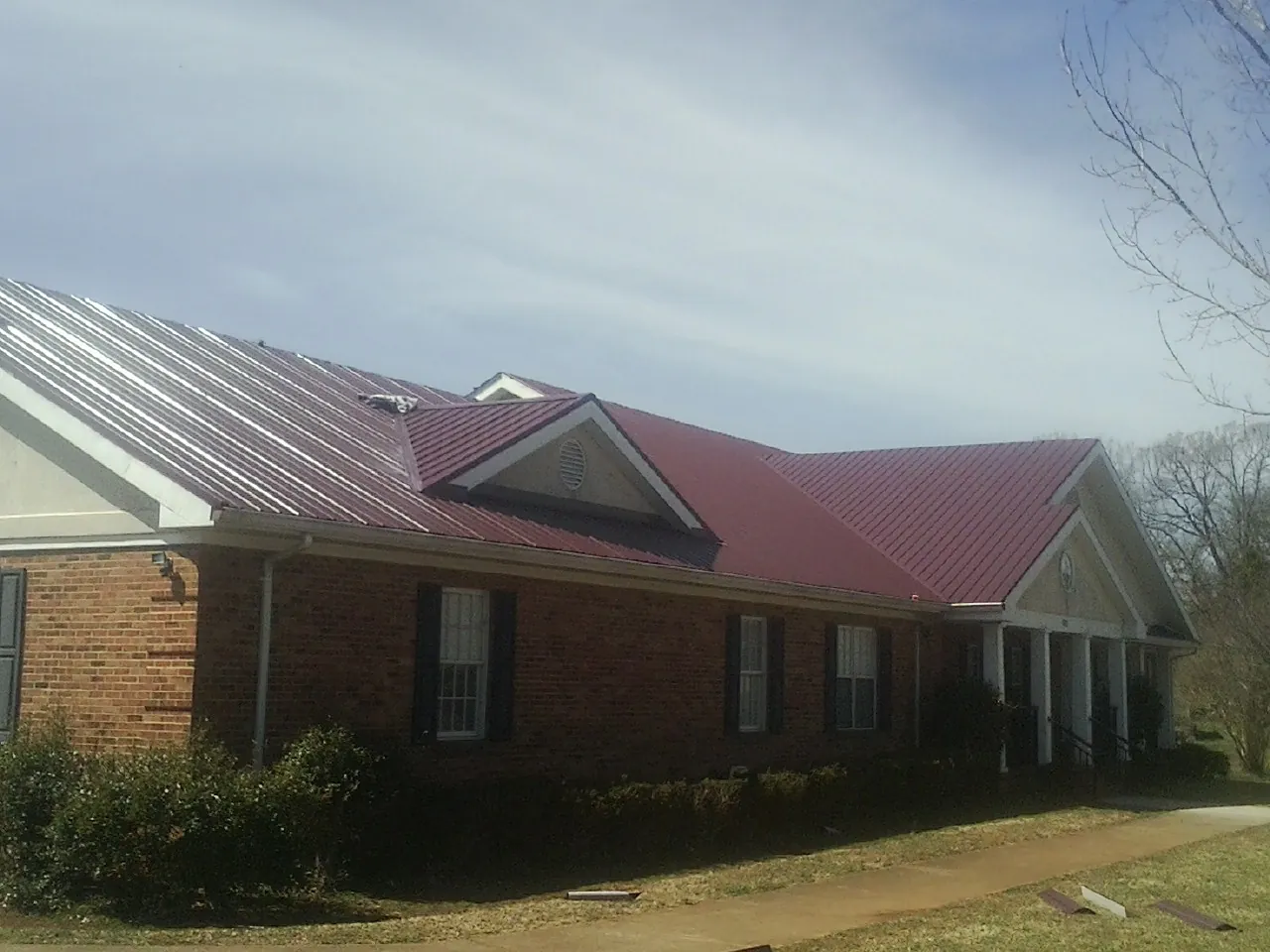 Red metal roof with gabled entries on a long brick building, from a Hail Damage Roof Repair job in Oquawka