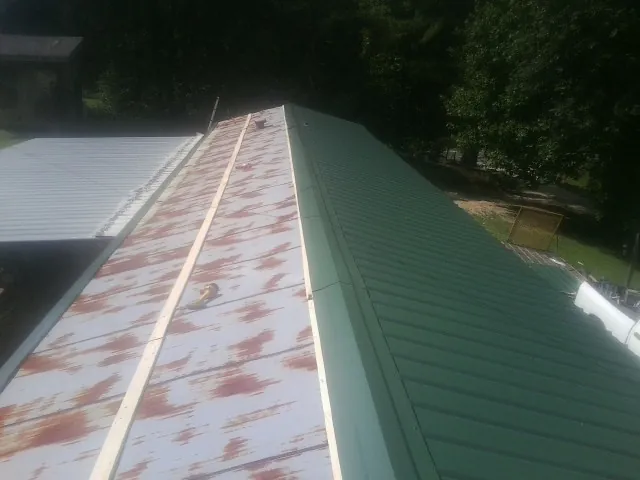 Old rusted panels beside newly installed green metal roofing — Wind Damage Roof Repair by Roofing Brothers in Oquawka
