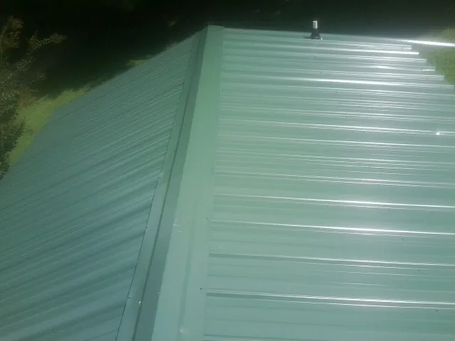 New green metal panels meeting at the ridge of a roof — Flat Roof Repair work by our crew in Oquawka