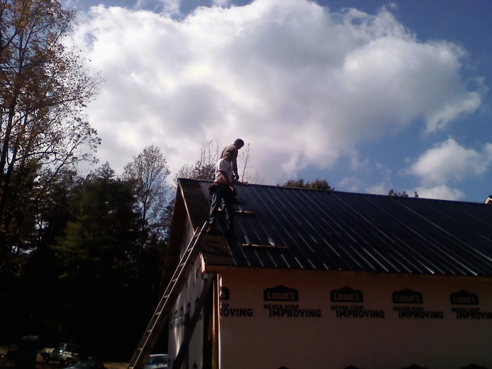 Roofer fastening dark metal panels high against a cloudy sky, from a Roof Inspection job in Oquawka