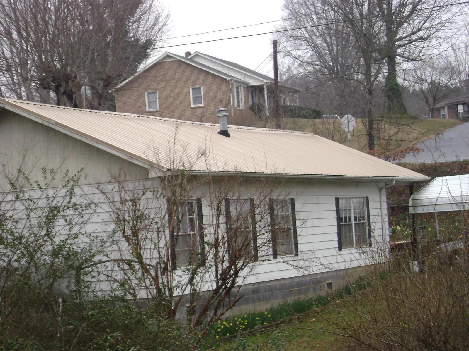 Tan metal roof on a white sided house set into a hillside — Commercial Roofing by Roofing Brothers in Oquawka