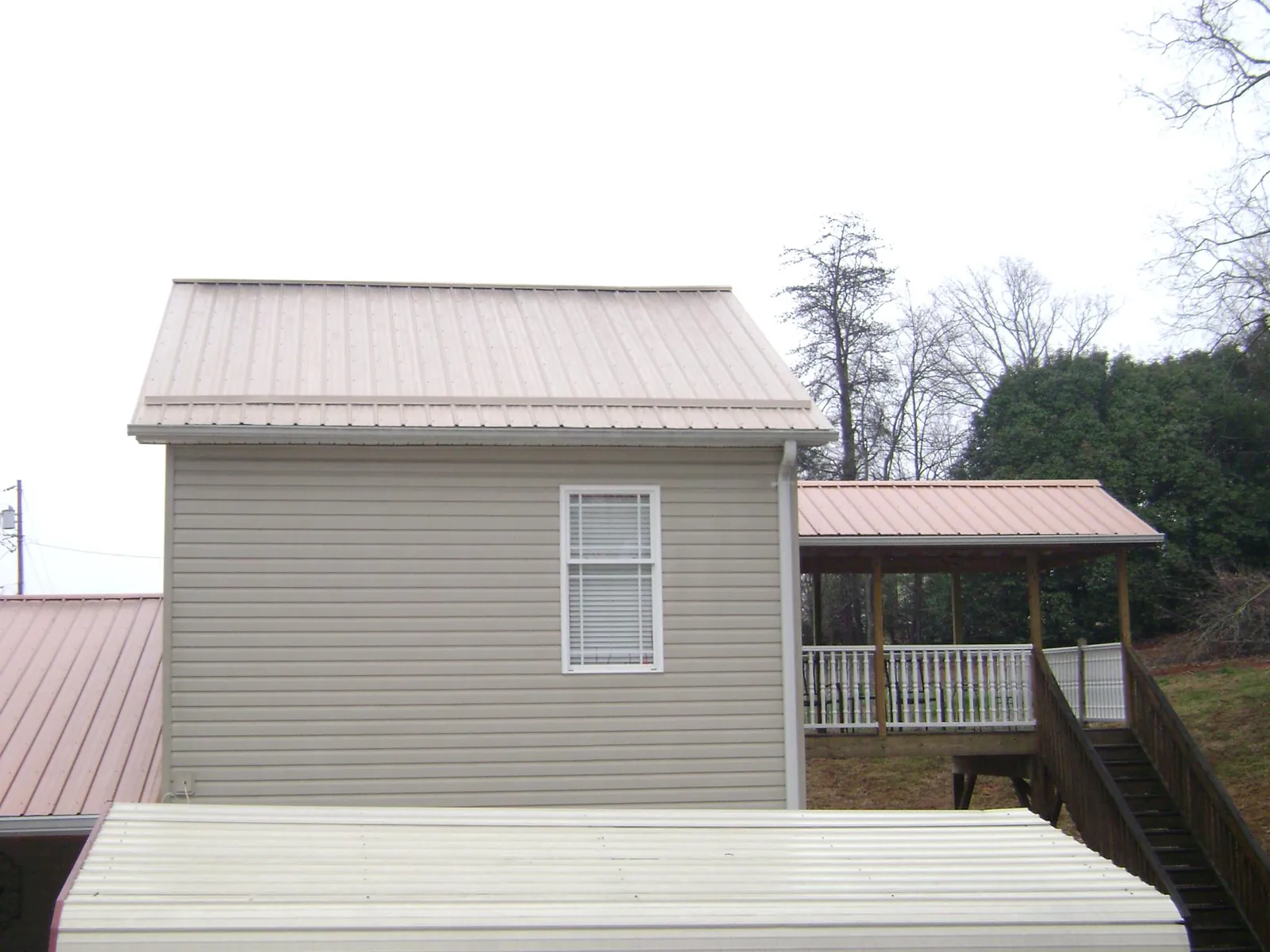 Tan metal roofs on a two story addition and attached porch, from a Roof Replacement job in Oquawka